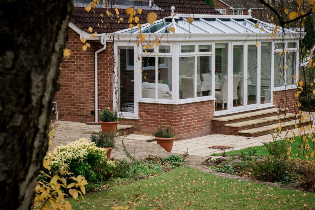 Ultraframe Conservatory in white on a red brick house in autumn